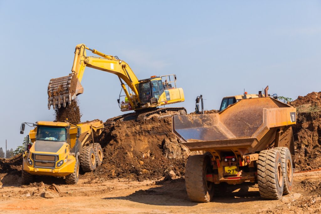 Excavators loading dump trucks on a construction site, representing heavy civil construction activities.